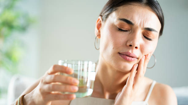 Young woman with sensitive teeth and hand holding glass of water stock photo