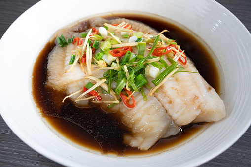 A plate of steamed tilapia fish with accompanying sauce. Garnished with ginger, chili and spring onions. A very popular dish in South East Asia.