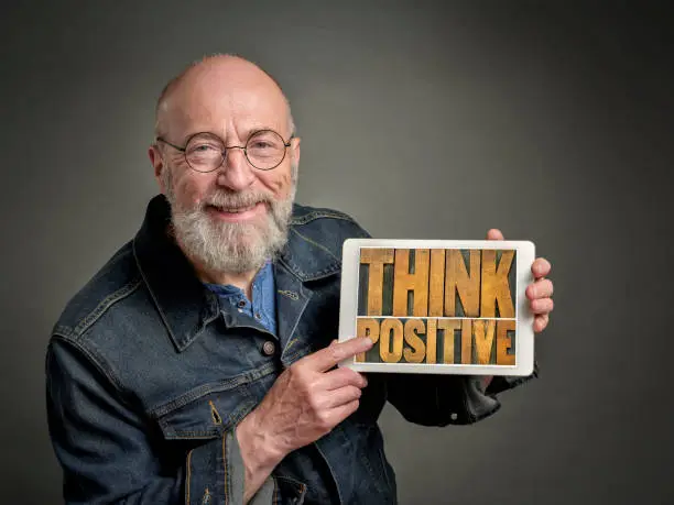 smiling senior man is showing a digital tablet with think positive sign in retro letterpress wood type, optimism and attitude concept