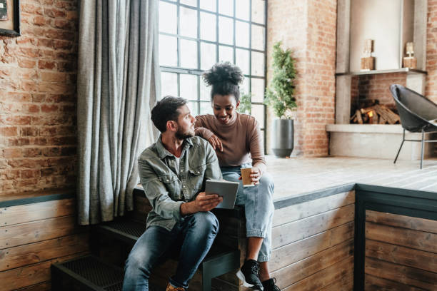 pareja multirracial en loft moderno utilizando tecnologías. pareja usando tableta digital para aplicaciones de hogar inteligente, banca electrónica y jugando videojuegos juntos. - banca electrónica fotografías e imágenes de stock