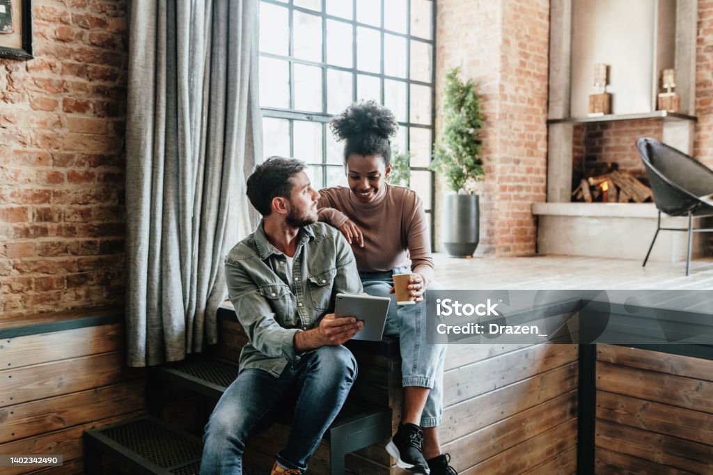 Multiracial couple in modern loft using technologies. Couple using digital tablet for smart home apps, electronic banking and playing video games together. Multiracial couple in modern loft Home Ownership Stock Photo