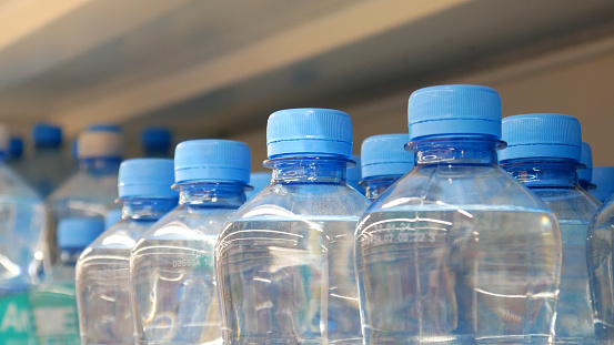 Many blue plastic bottles with drinking water on a store shelf close-up