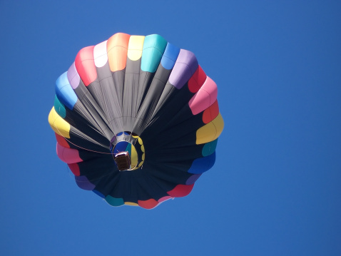 Colorful hot-air Balloon aloft, in blue sky.