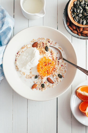 Oatmeal with curd cheese and tangerine on a white plate standing on a table