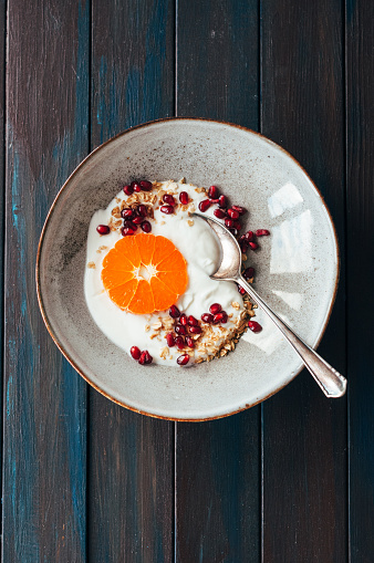 Oatmeal with yogurt, pomegranate and tangerine on a wooden table