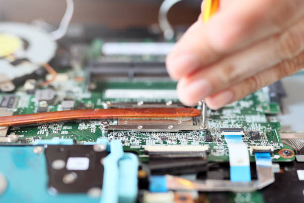 expert is repairing to inner of laptop with screwdriver. a laptop's central processing unit (cpu) has advanced power-saving features and produces less heat than one intended purely for desktop use. - service electronics industry circuit board capacitor imagens e fotografias de stock