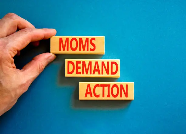 Photo of Moms demand action symbol. Concept words Moms demand action on wooden blocks on a beautiful blue table blue background. Businessman hand. Business, finacial and Moms demand action concept.