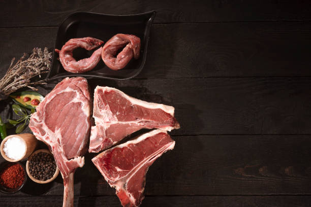 Meat raw steaks lie on a black background with vegetables, tomatoes, marasmade, mushrooms. background
