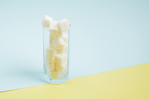 sugar cubes in a glass on a blue and yellow background copy space Too much sugar in drinks concept