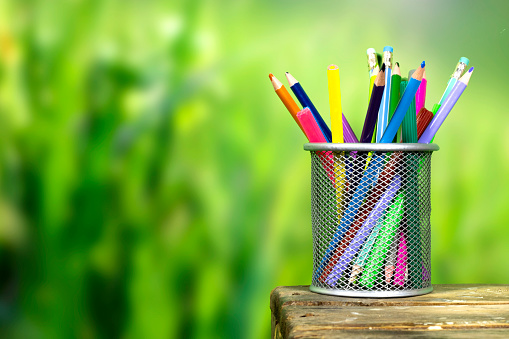 Colored pencils in a pencil case on  wooden board over nature blur grass, park background