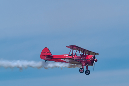 Hillsboro, Oregon, USA - May 22, 2022 :  Vicky Benzing, PhD and 1940 Boeing Stearman aerobatic airplane flying with a white trail of smoke. The Air Show in Hillsboro, Oregon is a very popular event each year. The theme for 2022 was “She Flies with her own wings.” All performers, pilots and announcers were women. Hillsboro is a suburb of the city of Portland, Oregon.