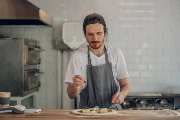 istock Man worker in a pizza place placing ingredients on pizza dough 1402360397