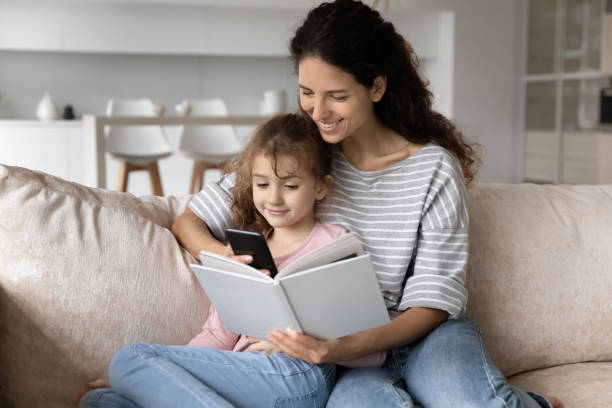 istock Smiling mother with daughter distracted from book, device addiction 1402361653