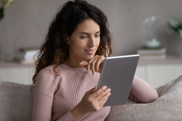 istock Head shot of smiling woman using tablet, sitting on couch 1402362444