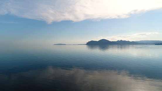 Beautiful reflection of blue sky in mirror water. Shot. Picturesque seascape with reflection of sky in sea on background of mountains. Morning blue sky is reflected in water surface.