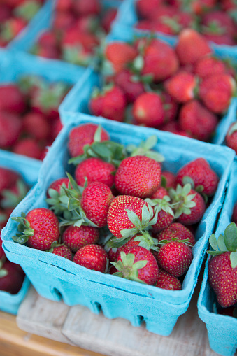 Small blue fruit cartons filled with fresh, ripe strawberries for sale at a farmer's market