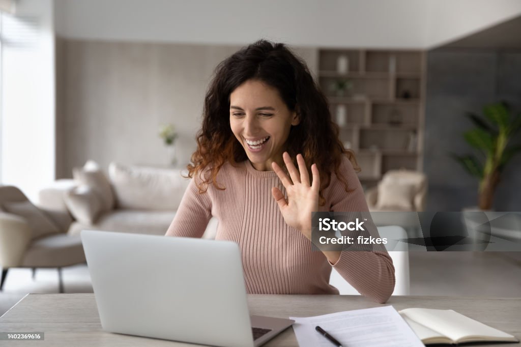 Smiling friendly hispanic businesswoman waving hand at laptop webcam Smiling friendly hispanic businesswoman waving hand at laptop webcam, greeting colleagues or friends, chatting online by video call, excited freelancer engaged in internet meeting conference Virtual Event Stock Photo