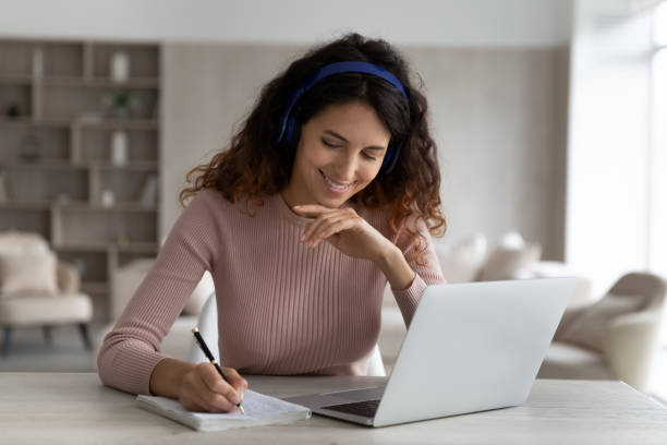 istock Head shot smiling woman in headphones taking notes watching webinar 1402369617