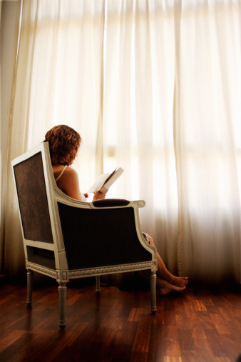 Woman reading her book in the light from the window.