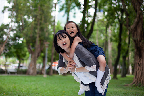 Asian little girl on a piggy back ride with her mother in park Taipei