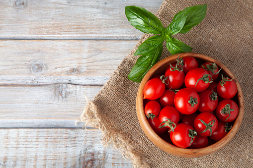 Fresh tomatoes in wooden bowl and basil on rustic wooden white table top view