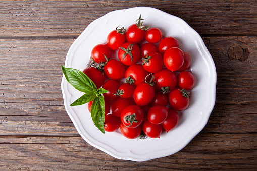 Fresh tomatoes in plate and basil on rustic wooden white table top view