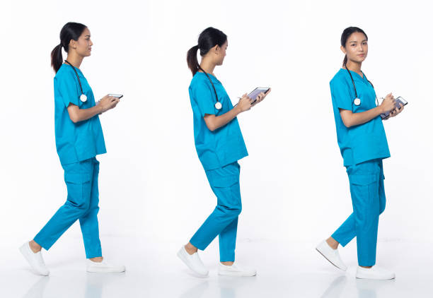 Full length 20s young Asian Woman clinic Nurse, walking forward left right Full length 20s young Asian Woman clinic Nurse, walking forward left right, wear blue dress pants shoes stethoscope. Smile Hospital female hold patient chart over white background isolated doctor utensils stock pictures, royalty-free photos & images