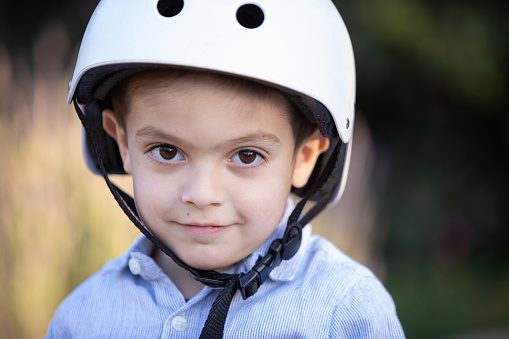 Cute 5 years-old boy playing outdoors with helmet and looking at camera