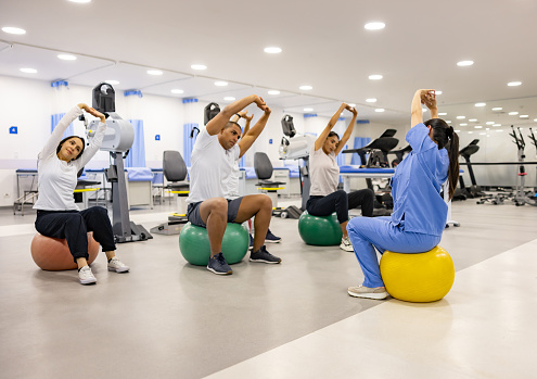 Group of patients following the instructions of their physical therapist while doing exercises on fitness balls at a rehabilitation center