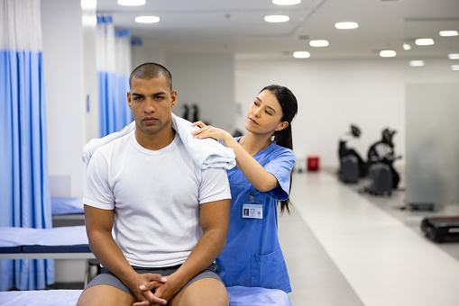 Physiotherapist putting an ice pack on a man with a shoulder injury at a rehabilitation center