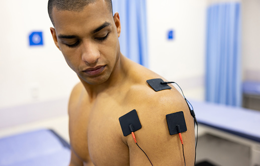 Young Latin American man in physiotherapy getting electrical stimulation therapy on his shoulder at a rehabilitation center