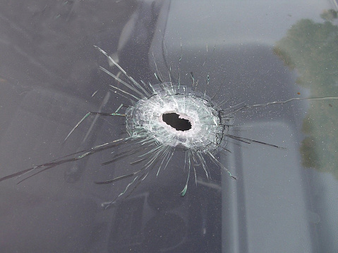 A close up photo of a bullet hole in a windshield of a car.