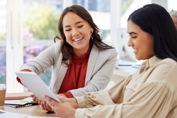 Team of two smiling business women using a digital tablet for a brainstorm meeting in the office. Happy confident ethnic professionals using technology while talking and planning a marketing strategy equipo de dos mujeres de negocios sonrientes que usan una tableta digital para una reunión de lluvia de ideas en la oficina. profesionales étnicos seguros y felices que usan la tecnología mientras hablan y planifican una estrategia de marketing