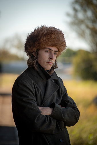 Young man in Russian Fur hat waits for a friend on an abandoned railway platform.