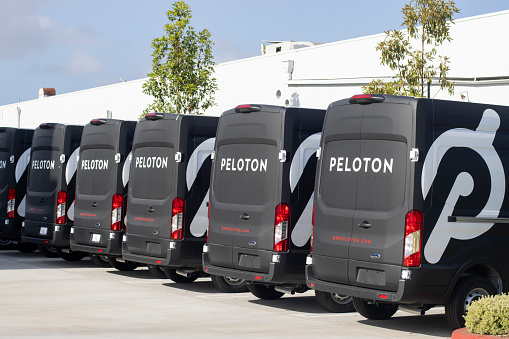 Santa Ana, CA, USA - May 9, 2022: Peloton branded delivery vans made by Ford Motor Company are seen in a parking lot outside a Peloton facility in Santa Ana, California. Peloton Interactive, Inc. is an American exercise equipment and media company based in New York City. Peloton's main products are Internet-connected stationary bicycles and treadmills that enable monthly subscribers to remotely participate in classes via streaming media.