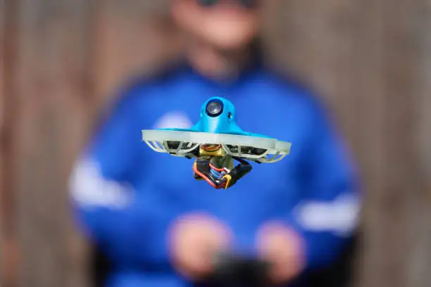 Photo of Small drone also race quad in blue is precisely controlled by the human pilot, wall in brown as background. Germany.