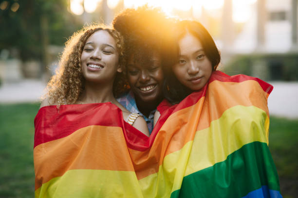 gruppe multirassischer freundinnen mit mehrfarbiger gay-pride-flagge, glückliche lesbische frauen bei sonnenuntergang im park - bi sexual stock-fotos und bilder