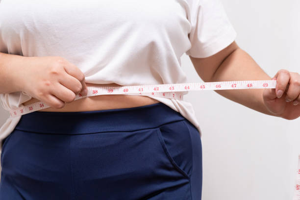 nahaufnahme von frauen, während sie maßband mit ihrem bauch oder hüftbauch von molligen frauen verwenden, die anzeichen von übergewicht zeigen. auf weißem hintergrund mit kopierraum für text - overweight tummy tuck abdomen body stock-fotos und bilder