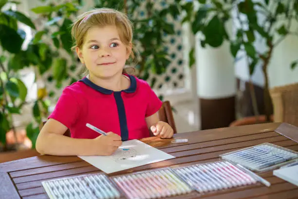 Happy preschool girl learning painting with colorful pencils and felt pens. Little toddler drawing at home on sunny summer day, using colorful feltpens. Creative activity for children