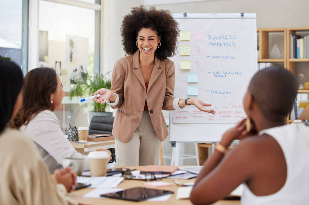 istock Mixed race businesswoman with afro using whiteboard for staff training in office workshop. Hispanic professional standing and teaching team of colleagues. Sharing ideas and planning marketing strategy 1402421131