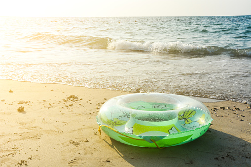 green inflatable round tube, plastic swim ring on the sand beach with sunlight in the evening