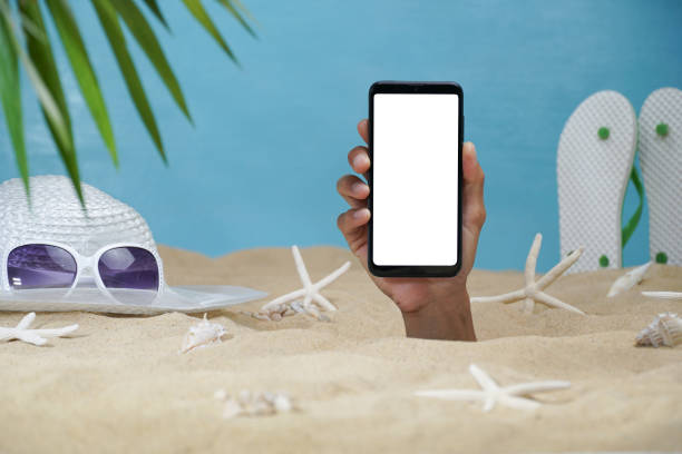 istock Hand holding a smart phone with white spcae through a sand beach. for creating media on smart phone. 1402433928