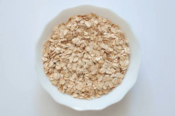 Top view of healthy and nutritious natural oat flakes in white bowl. Popular cereal food isolated on white background, selective focus.