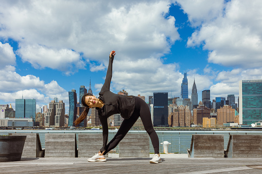 Asian girl exercising outdoors. She is at Long Island City, East river coast, New York city. Manhattan skyline in the background