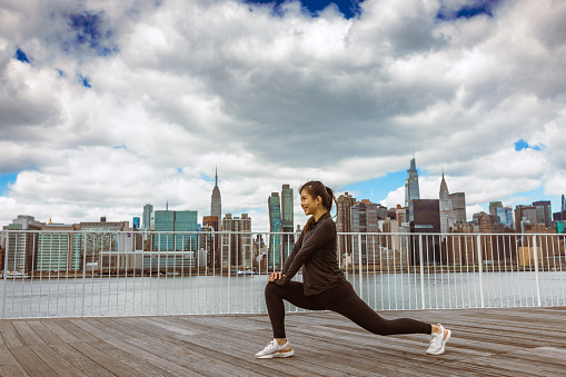 Asian girl exercising outdoors. She is at Long Island City, East river coast, New York city. Manhattan skyline in the background
