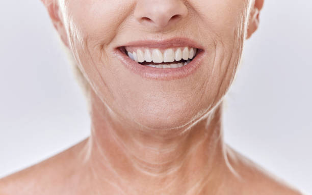 happy mature caucasian woman with a bright smile, showing her natural looking veneers while posing against a purple copyspace background. older woman happy with her oral hygiene while doing skincare - half smile imagens e fotografias de stock