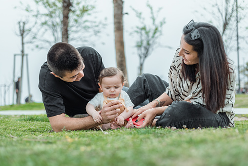 Parents with baby boy in public park. Cheerful family having fun on grass in public park for weekend.