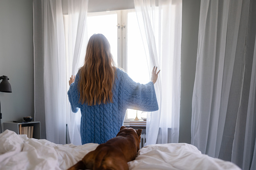Young woman at home in her bedroom on a weekend morning. She is in bed together with her pet dog.