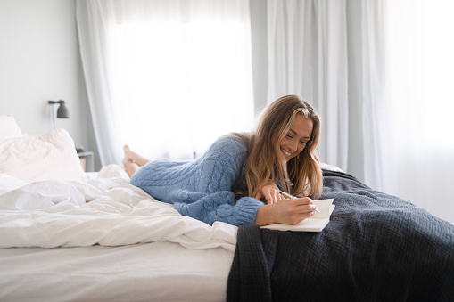 Young woman at home in her bedroom on a weekend morning. She is writing in her daily diary.