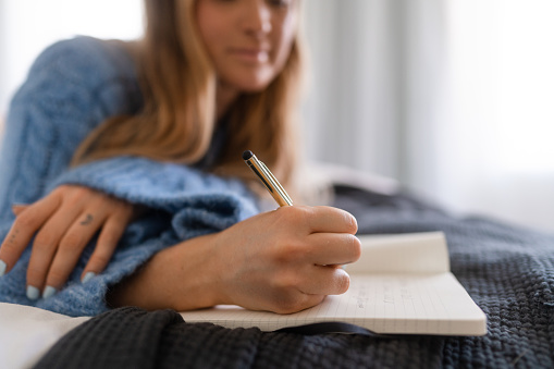Young woman at home in her bedroom on a weekend morning. She is writing in her daily diary.